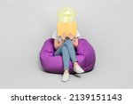 Female body of model with bright electric bulb instead head read book sit bean bag isolated on grey color background modern design learn concept