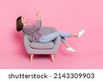 Profile side view portrait of attractive cheerful girl sitting in armchair using device isolated over pink pastel color background