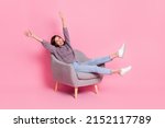 Portrait of attractive cute cheerful girl sitting in armchair rising hands up isolated over pink pastel color background