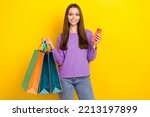 Photo of young positive glad influencer woman hold her bags with clothes black friday big sale hold smartphone eshopping isolated on bright yellow color background