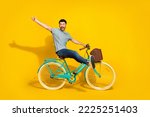 Small photo of Side profile photo of funky crazy excited man wear gray t-shirt denim jeans sitting new retro bicycle raise palm hello friends isolated on yellow color background