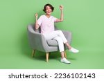 Photo of positive pretty lady wear trendy stylish outfit sit comfy chair raise arm hand rejoice enjoy isolated on green color background
