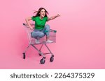Full length photo of pretty excited lady dressed green t-shirt riding shopping cart empty space isolated pink color background