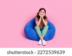 Full body length photo of young stressed sit bean bag unhappy minded bored woman touch cheekbones look empty space isolated on pink color background