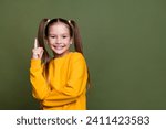 Small photo of Portrait of smart clever small kid with tails dressed yellow sweatshirt raising finer up has idea isolated on khaki color background