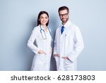 Two best smart professional smiling doctors workers in white coats holding their hands in pockets and together standing against gray background