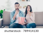 Small photo of Unexpected turn of events in a film! Two charming beautiful funny man with bristle clothed in jeans denim outfit and attractive dressed in sweater and jeans woman are pop-eyes surprised watching tv