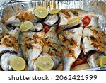 Small photo of Seafood cuisine, sea bream fishes cooked in the oven with lime slices, tomatoes and onion rings in a foil plate, gilt-head bream fishes recipe, denise fish cooked, selective focus