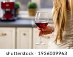 Unrecognizable blonde woman standing with glass of wine in kitchen