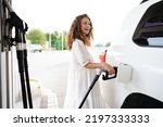 Young curly woman refueling car at gas station