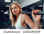 Small photo of Middle-aged fitness woman doing squat exercise in a gym