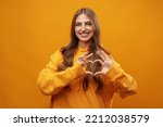 Young pretty woman smiling and making heart sign with both hands on yellow background