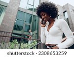Small photo of Young smiling african woman using smartphone going downstairs in the city