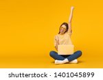 Winner! Excited smiling girl sitting on floor with laptop, raising one hand in the air is she wins, isolated on yellow background