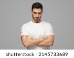 Small photo of Serious young man portrait. Tough guy standing with crossed arms isolated on grey background