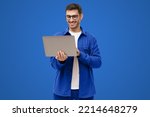 Young man holding laptop surfing, browsing online, typing message or watching movie isolated on blue background
