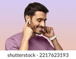 Young man wearing wireless earbuds and purple tshirt, listening to his favorite musical album online, touching one earphone to control application