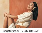 Profile view studio shot of relaxed asian woman with wireless headphones, listening to meditation music with closed eyes, smiling with pleasure after work day