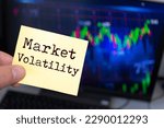 Male hand holding sticky note written Market Volatility.