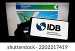 Small photo of Stuttgart, Germany - 09-07-2022: Person holding mobile phone with logo of Inter-American Development Bank (IADB) on screen in front of business web page. Focus on phone display. Unmodified photo.