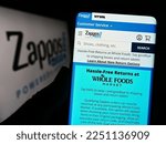 Small photo of Stuttgart, Germany - 01-13-2023: Person holding cellphone with website of US online shop company Zappos.com LLC on screen in front of logo. Focus on center of phone display. Unmodified photo.