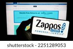 Small photo of Stuttgart, Germany - 01-13-2023: Person holding mobile phone with logo of American online shop company Zappos.com LLC on screen in front of web page. Focus on phone display. Unmodified photo.