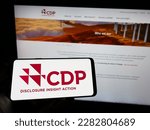Small photo of Stuttgart, Germany - 03-25-2023: Person holding cellphone with logo of organization Carbon Disclosure Project (CDP) on screen in front of webpage. Focus on phone display. Unmodified photo.