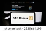 Small photo of Stuttgart, Germany - 07-11-2023: Person holding cellphone with logo of expense management software SAP Concur on screen in front of business webpage. Focus on phone display. Unmodified photo.