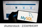 Small photo of Stuttgart, Germany - 07-13-2023: Person holding cellphone with logo of relational database management system MySQL on screen in front of webpage. Focus on phone display. Unmodified photo.