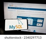 Small photo of Stuttgart, Germany - 07-13-2023: Person holding mobile phone with logo of relational database management system MySQL on screen in front of web page. Focus on phone display. Unmodified photo.