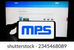 Small photo of Stuttgart, Germany - 08-05-2023: Person holding cellphone with logo of American company Monolithic Power Systems Inc. (MPS) on screen in front of webpage. Focus on phone display. Unmodified photo.