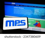 Small photo of Stuttgart, Germany - 08-05-2023: Person holding mobile phone with logo of US company Monolithic Power Systems Inc. (MPS) on screen in front of web page. Focus on phone display. Unmodified photo.