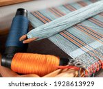 Small photo of Handloom with shuttle on the blue warp threads and two bobbins with indigo and orange yarns. Vertical stripe weave
