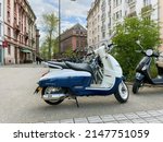 Small photo of Strasbourg, France - Apr 10 2022: Side view of new white blue Scooter Django Standard 125 by Peugeot Motocycles with French city of Strasbourg in background