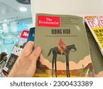 Small photo of London, United Kingdom - 21 Apr 2023: A male hand holds the latest issue of The Economist, featuring an illustrated cover story on Americas economy. Journalism and mass media join forces to inform the
