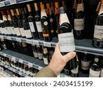 Small photo of Paris, France - Nov 10, 2023: POV of a male hand holding a bottle of French Madiran wine, vintage 2018, in a supermarket, highlighting a discerning wine choice