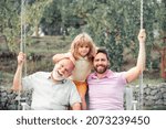 Boy son with father and grandfather swinging together in park outdoors. Three different generations ages grandfather father and child. Dad, son and granddad hugging.