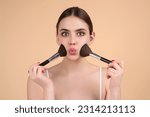 Small photo of Girl hold blush blusher apply powder visage isolated over studio background. Woman powdering cheeks. Makeup brush. Female model gets blush powder on the cheekbones.
