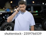 Small photo of Gangster call phone. Angry man chatting on phone near car on night urban street. Dangerous aggressive man with phone. Criminal city. Danger american district. Aggressive angry man talking on phone
