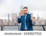 Small photo of Businessman with dollars money. Excited man with dollar money on street. Rich business man in suit hold dollar cash. Businessman hold 100 dollars banknotes at city. Dollars banknote.