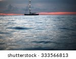 Small photo of Beautiful calm evening seascape with silhouette of yacht under bare poles floating in blue sea waves after red sunset in background on the horizon distant view, horizontal picture