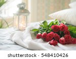 A bunch of pink roses on white crochet cardigan, white pillows, small silver lamp and tree at background, a surprise Valentine's Day in bed, soft color tone