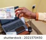 An african hand receiving Nigerian Naira notes, cash or currency with phone on a laptop in the background