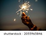 Small photo of Hand holding sparkler firework firing with sunset sky in background - concept of new year eve celebration people - hope and love image of woman dreams - warm tones