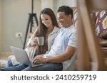 Small photo of Happy young relaxed couple sitting on sofa with laptop on laps, discussing funny movie, enjoying watching comedian film, shopping online or web surfing, full length front view, leisure pastime concept