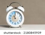 Small photo of Eleven o'clock on the alarm. A white alarm clock is on a white table. The clock hand points to 11 o'clock. Time to change to summer or winter time. Set an alarm for 11:00 or 23:00. copy space