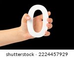 Small photo of Zero in hand. The number zero is clasped in a hand isolated on a black background. Number zero white in a child's hand on a black background.