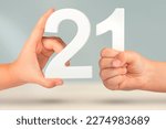 Small photo of Number two one in hand. Hand holding white number 21 on blurred background with copy space. Concept with number twenty one. 21 percent, birthday 21, twenty one