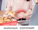 Small photo of woman sufferings from stomachache after overeating junk food pizza at the office desk hand holding her stomach that is full of gas, gerd from acid reflux