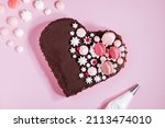 Top view of Pink heart shaped cake with chocolate glaze, meringues and macaroons on top as decoration. Placed on pink background. Valentine's day, mothers day, birthday, celebration concept.